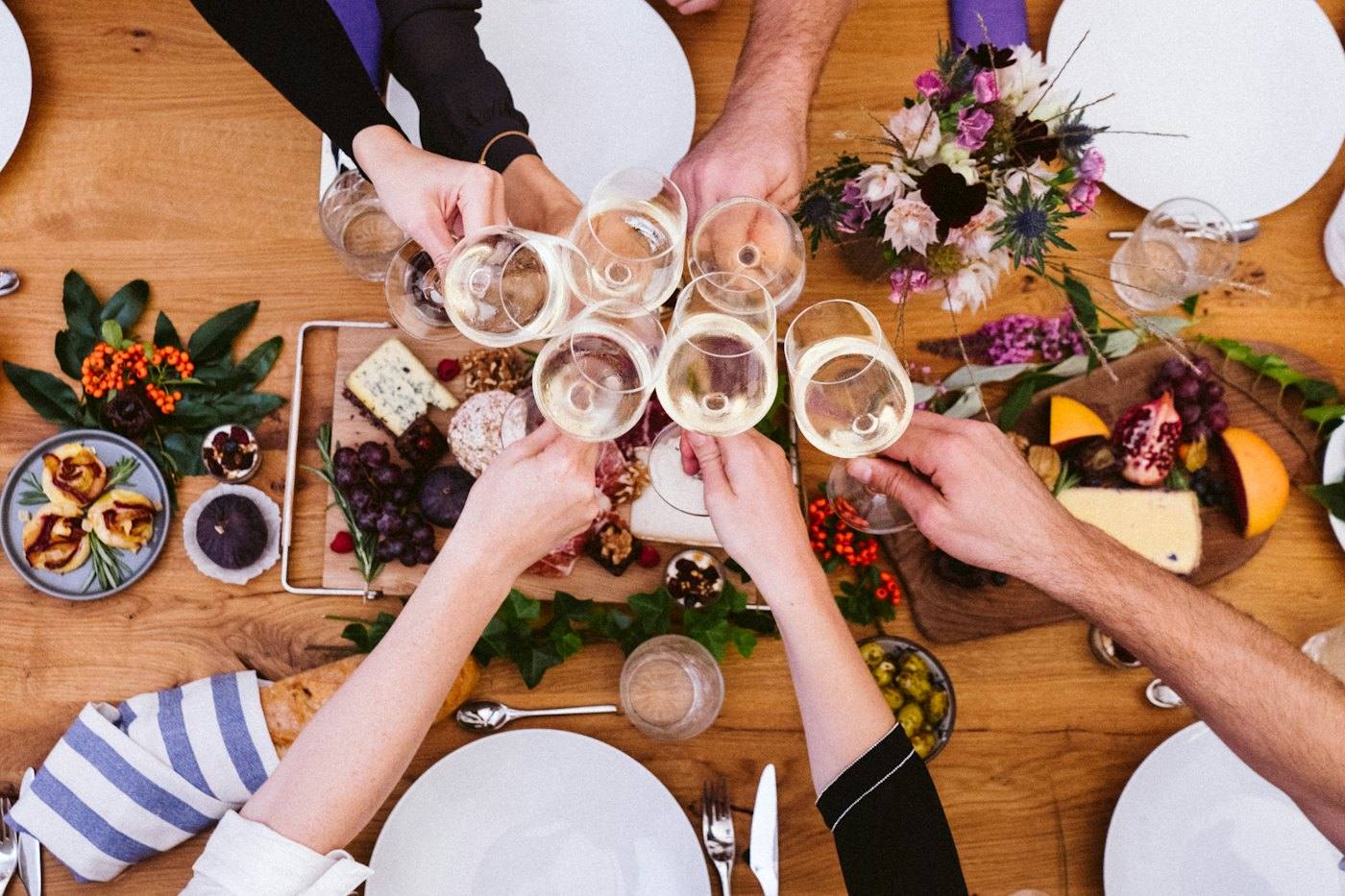 Many hands clinking glasses over a shared table